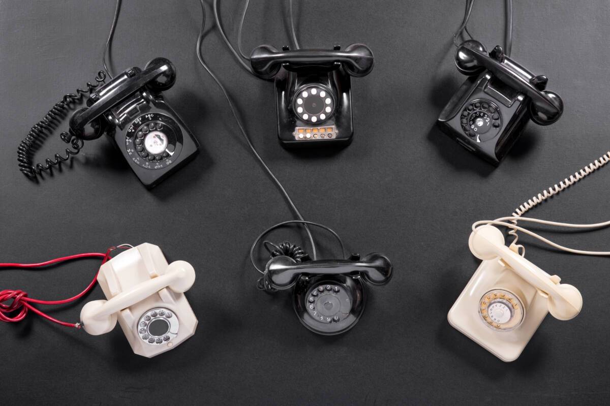 6 old vintage rotary dial up telephone instruments in white and black viewed from overhead on a dark gray background