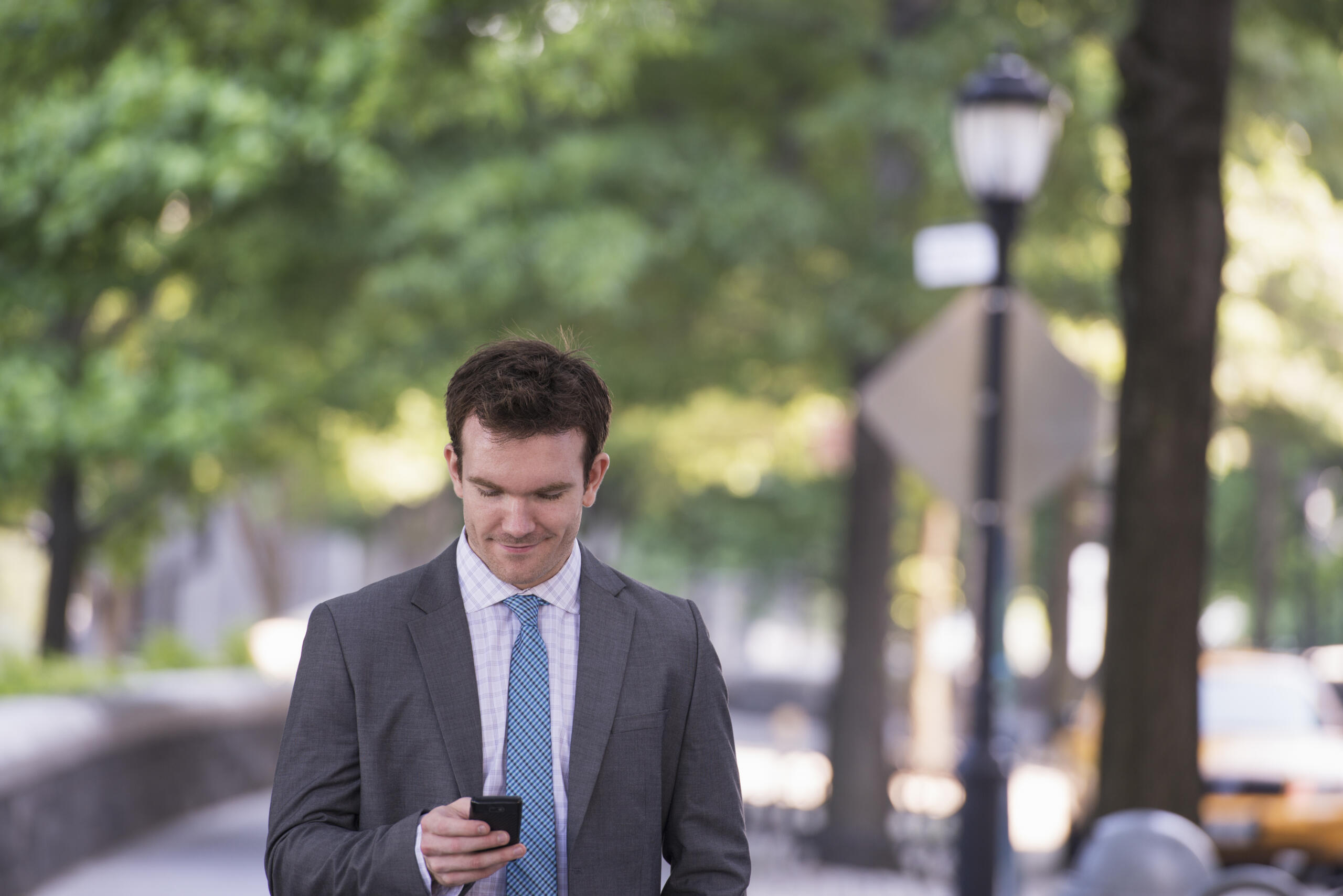 Attorney answering services: lawyer looks at his phone while walking outside on a sunny day