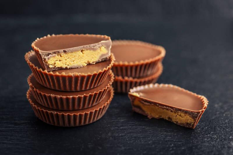 Close-up of peanut butter cups (candy), some stacked, some with bites taken out, on a dark gray background