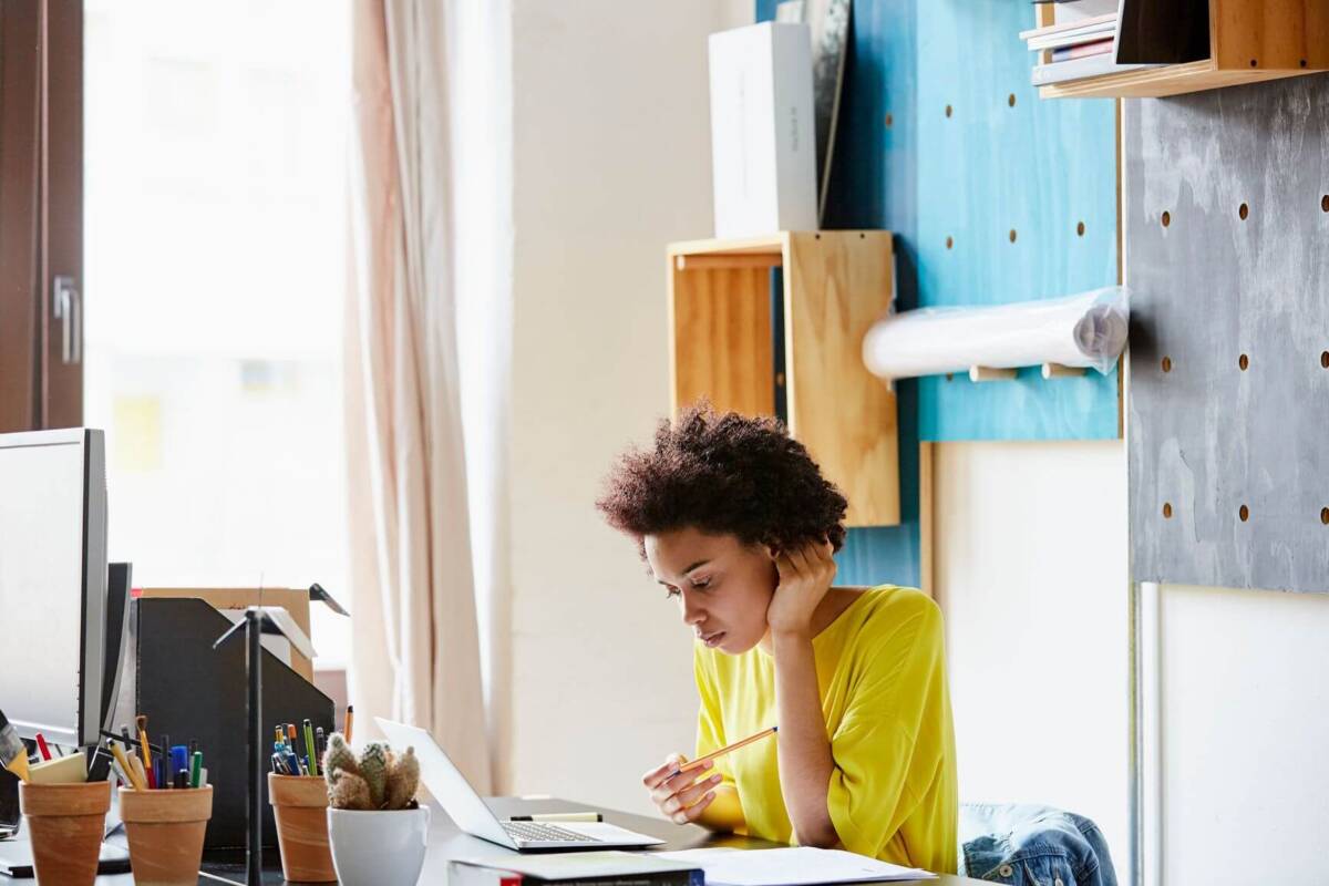 Woman sits at desk with her hand on the back of her head, looking concerned at laptop