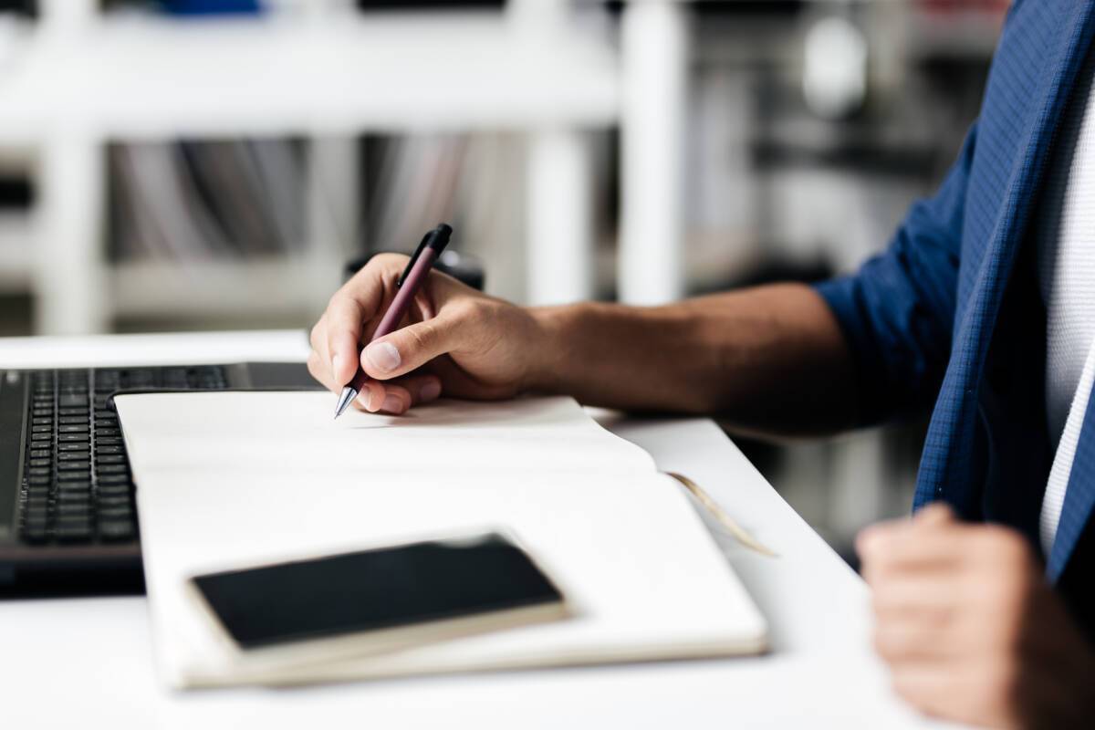 Man makes notes in a notebook on a table with a phone