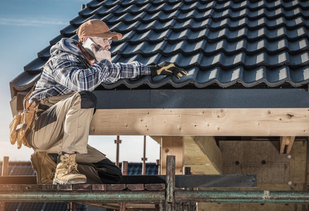 Caucasian Professional Roof Construction Worker in His 40s Making Phone Call While Staying on Scaffolding. Roofer Calling For Supply.