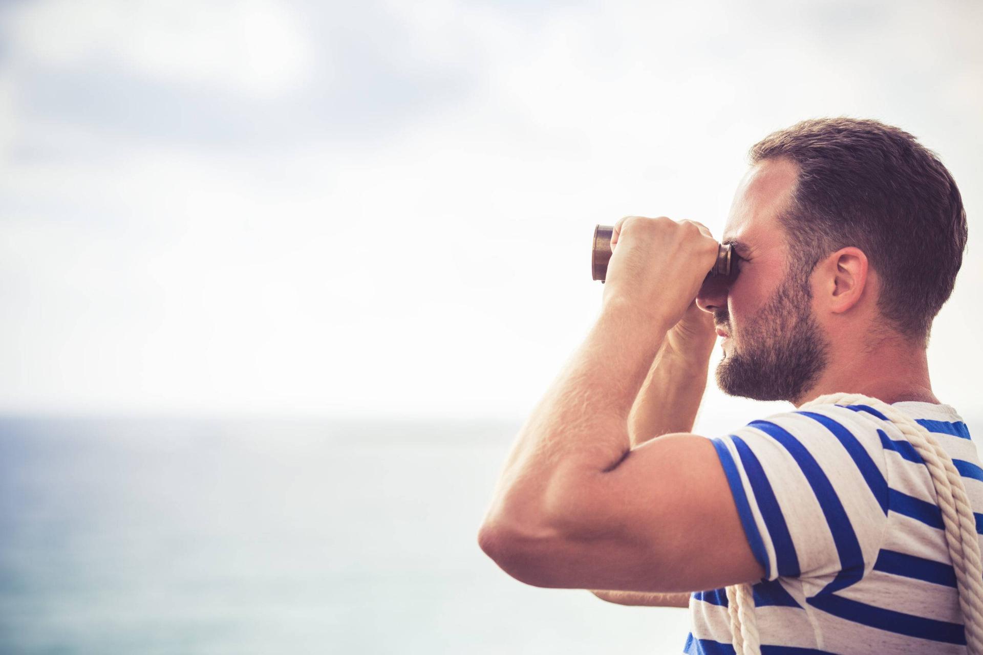 A man in a blue and white-striped shirt looks through binoculars at the open sea