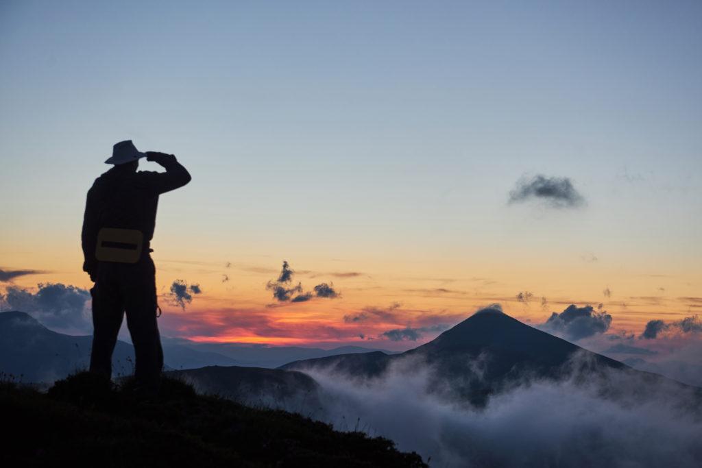 A man in silhouette looks out over a foggy mountain range