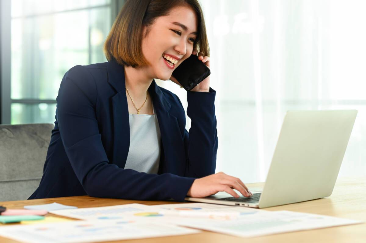 How to attract more law firm leads: smiling woman in professional attire talks on phone while using laptop