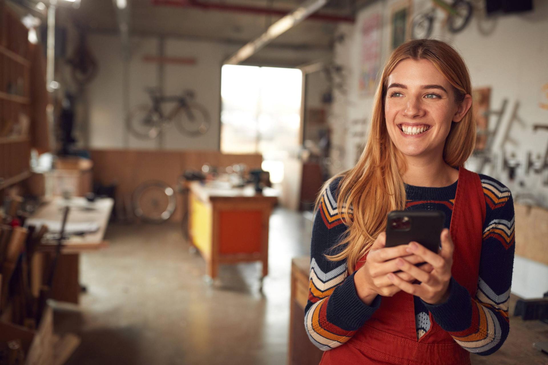 Smiling woman standing in a bicycle workshop with a mobile device in her hands