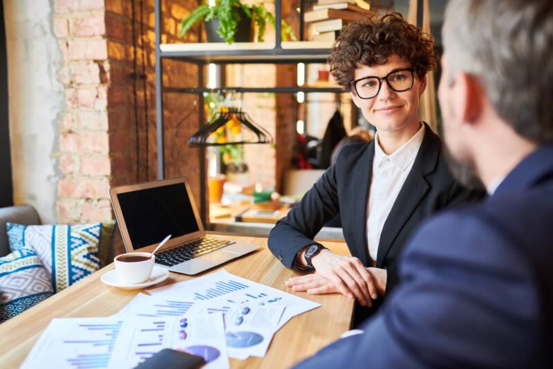 Why empathy matters for your business: person listening to another person in cafe with laptop, papers, and coffee