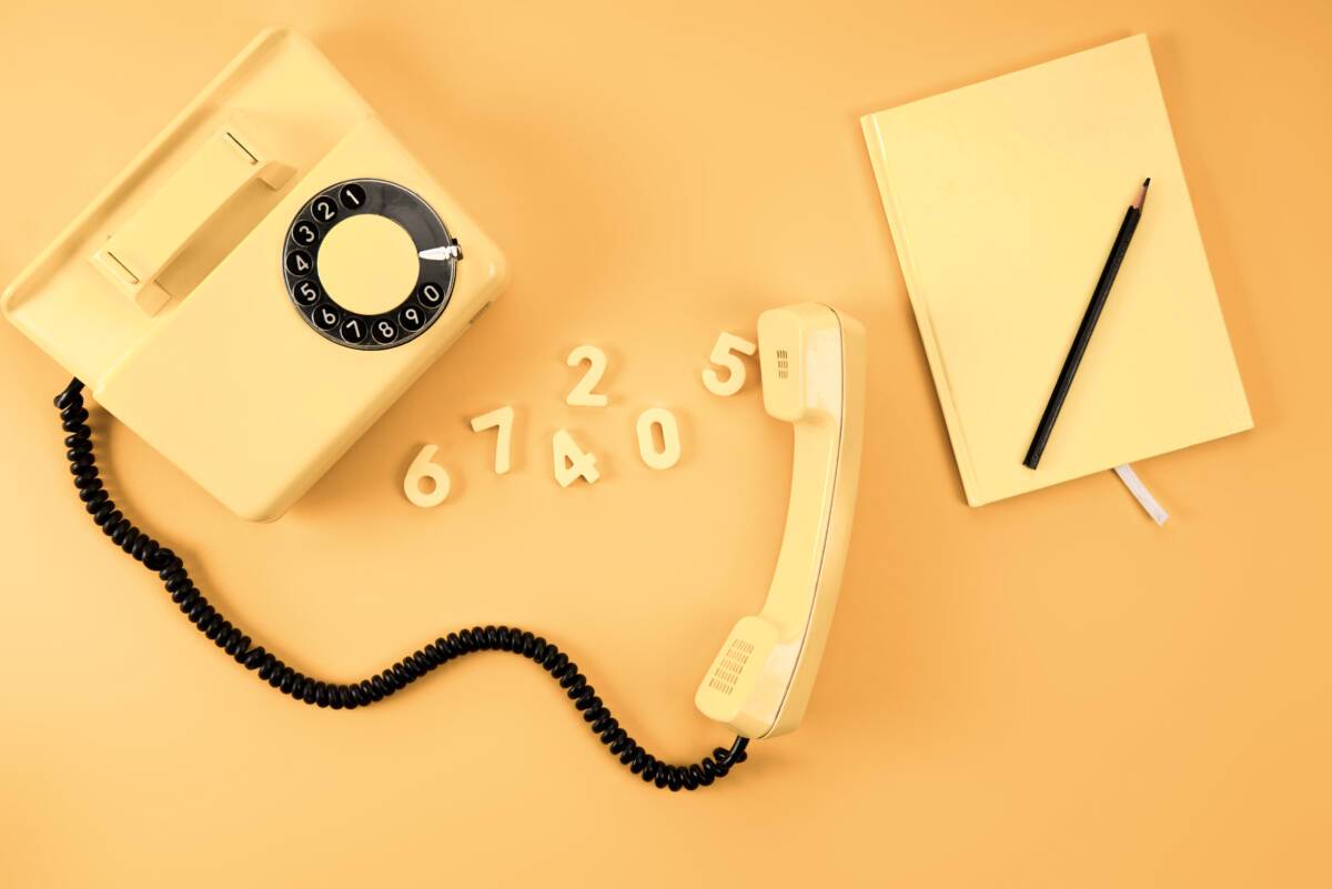 Choosing a business number: overhead view of faded yellow vintage telephone with notebook and numbers on monochrome background