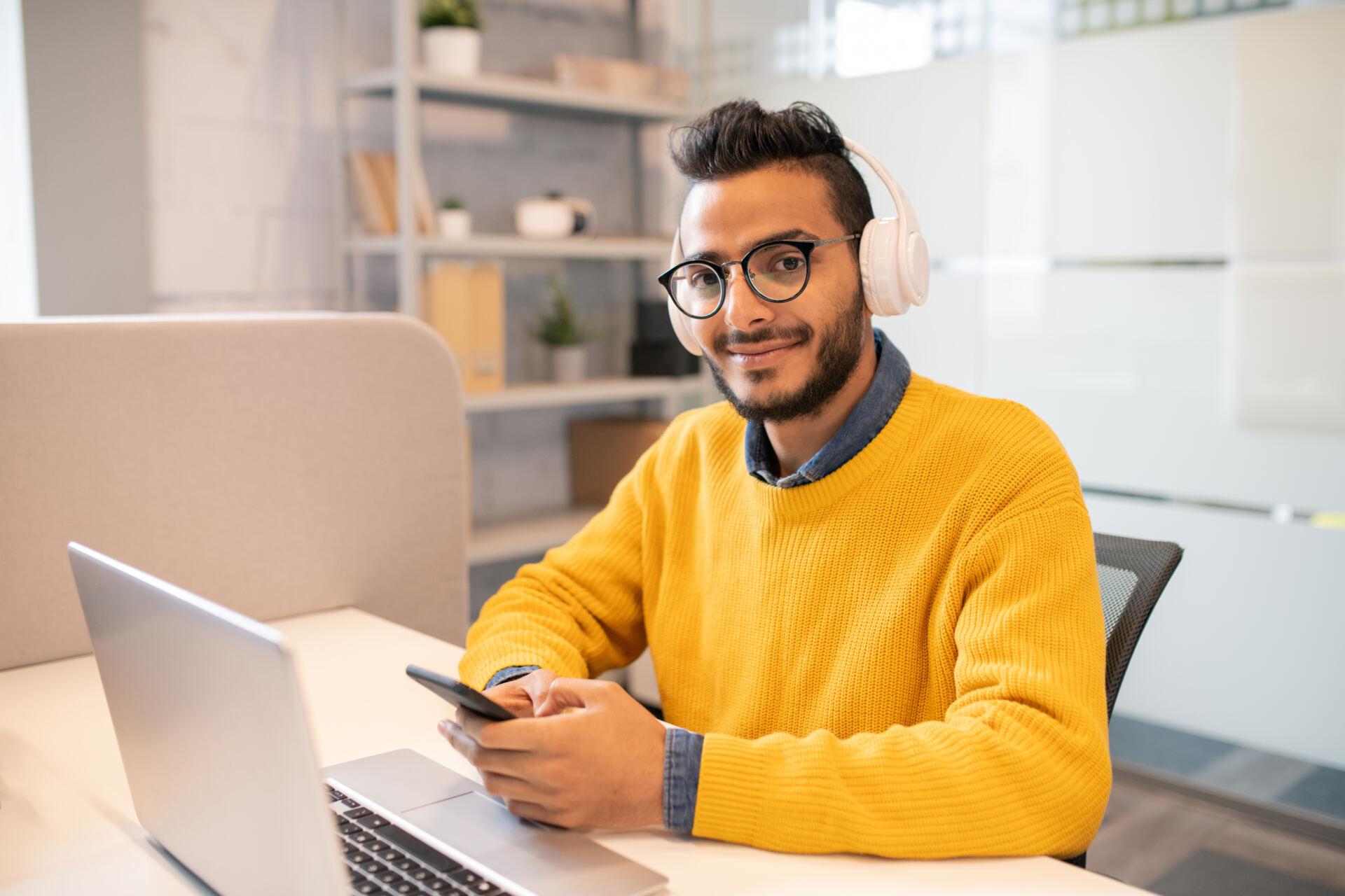 Creative professional sits at desk in front of laptop with phone in his hands