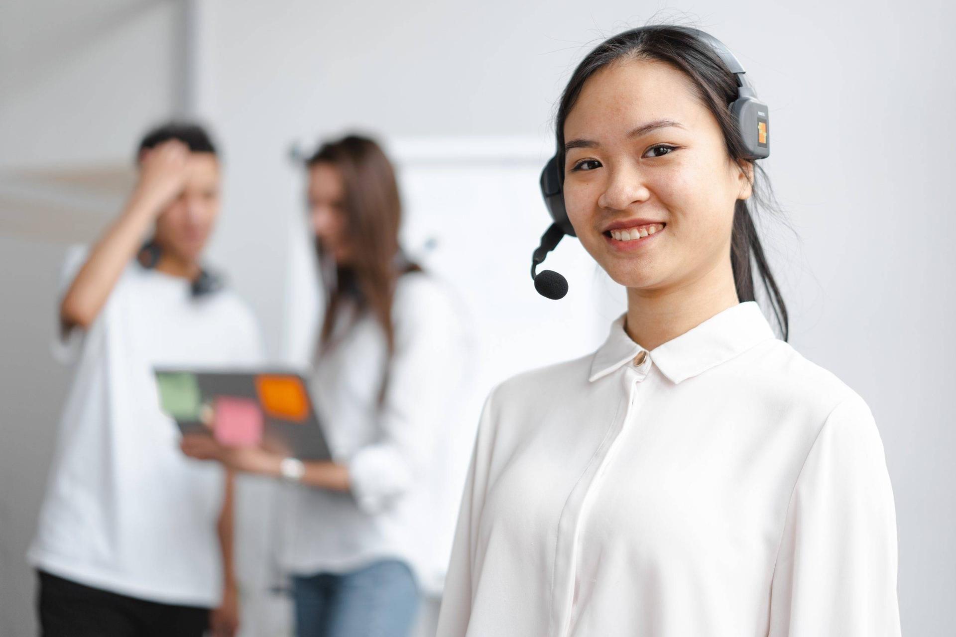 Virtual receptionist wearing headset stands in a white room as two people have a conversation in the background