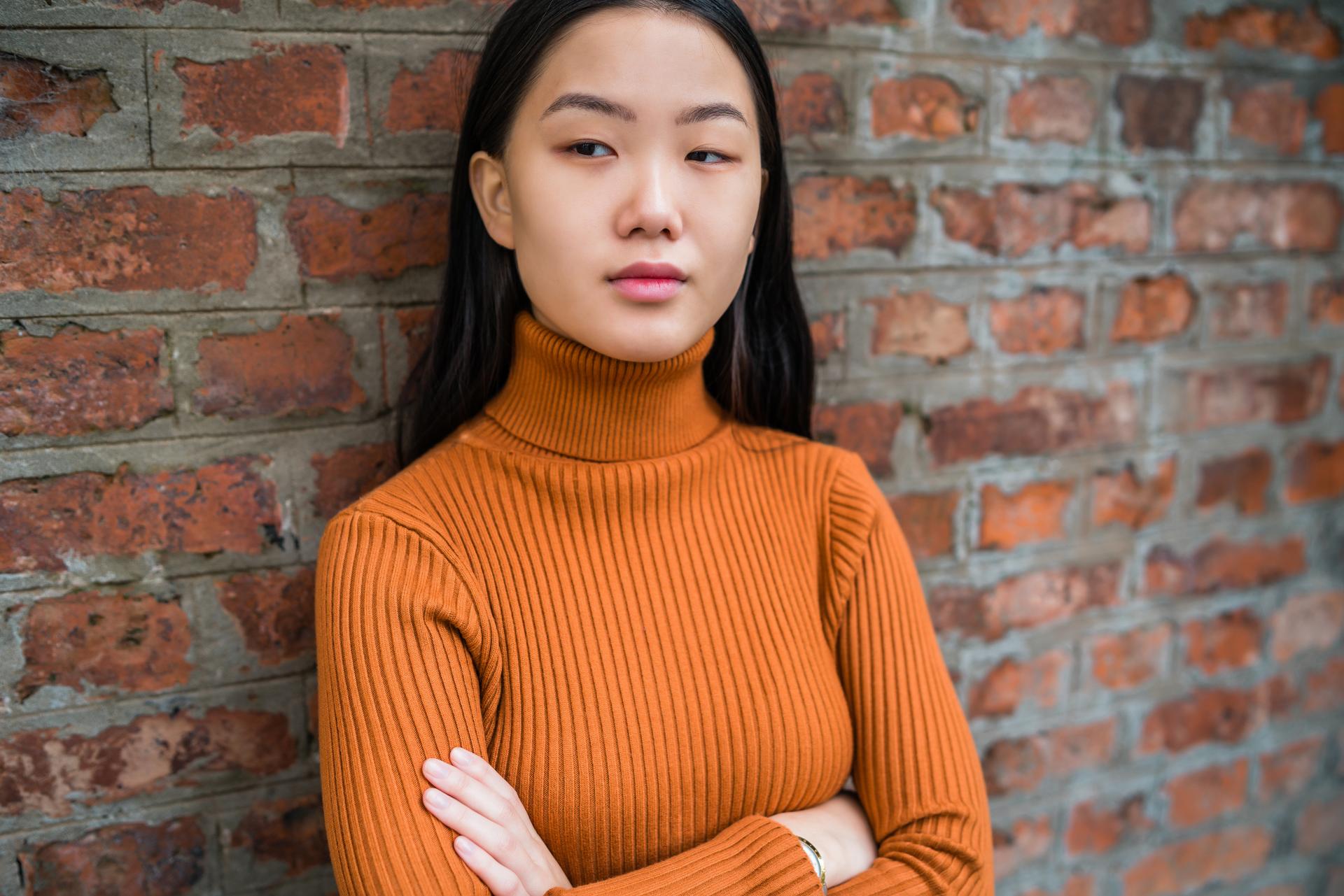 Tiffany stands in front of a brick wall with her arms folded