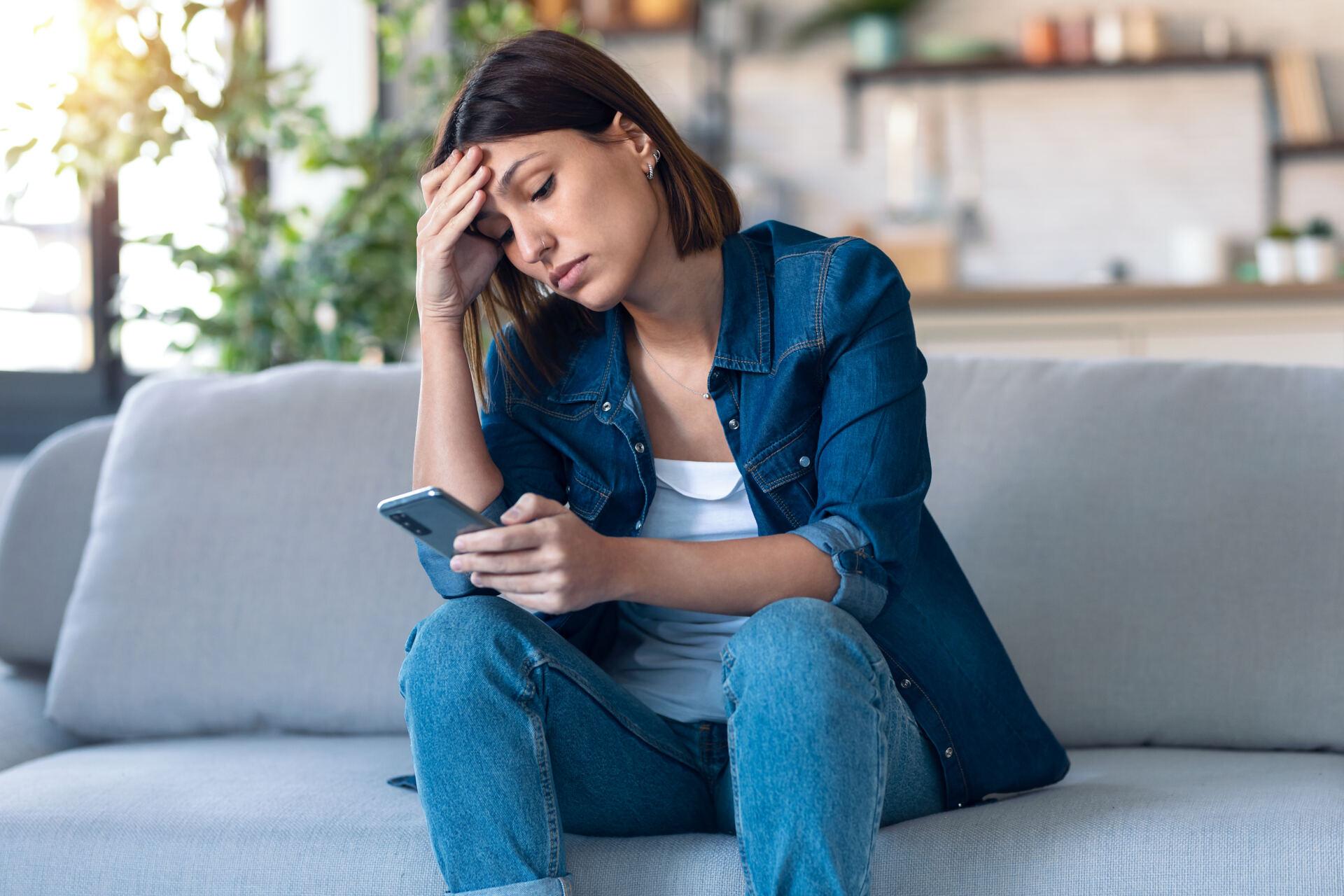How much time is your business losing to robocalls: worried person using their mobile phone while thinking about problems sitting on couch in the living room at home