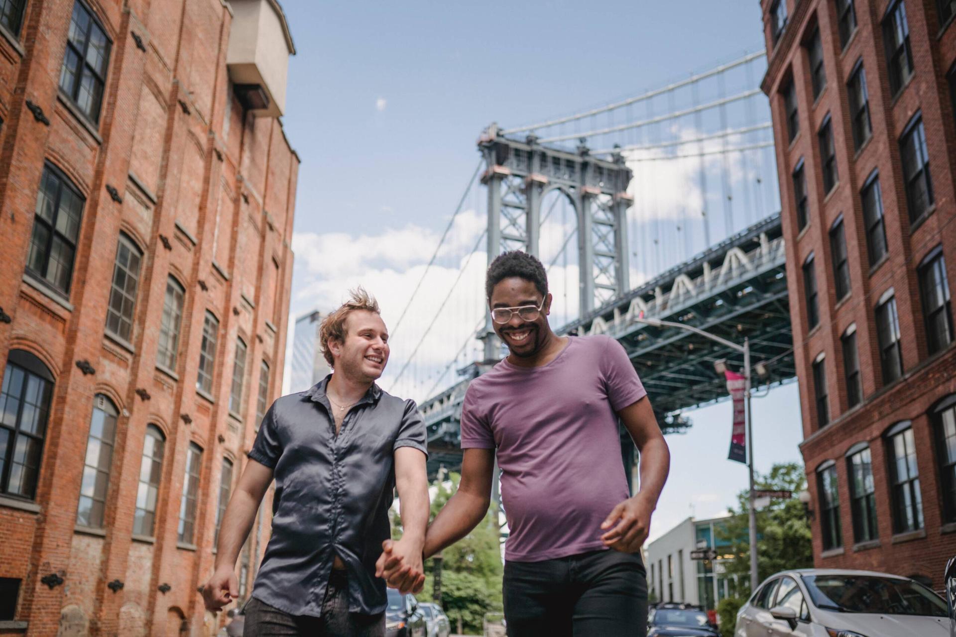 Two smiling men holding hands and walking through a city