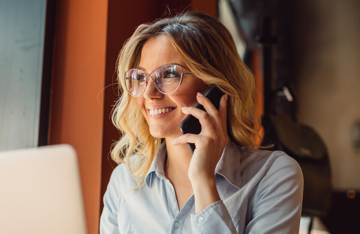 Woman with glasses in cafe using laptop and talking on phone