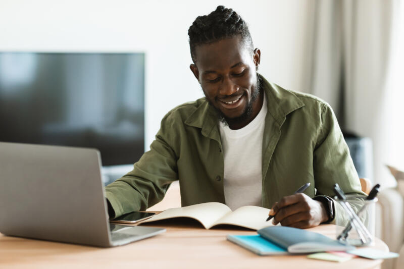 Business website checklist: smiling man in front of laptop looks at notebook on desk