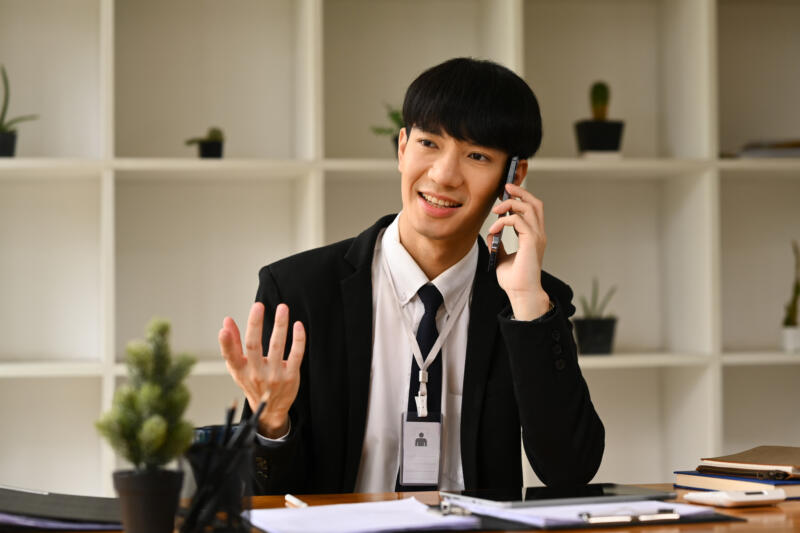 Call screening: smiling man in suit sits in sparse office talking on the phone while gesturing with free hand