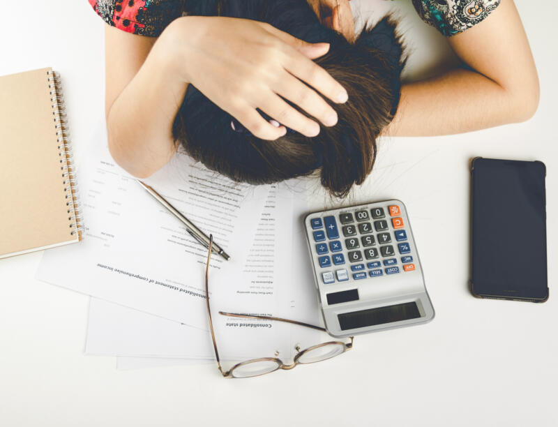 Why isn't my business making enough money: stressed woman slumps over calculator and financial paperwork