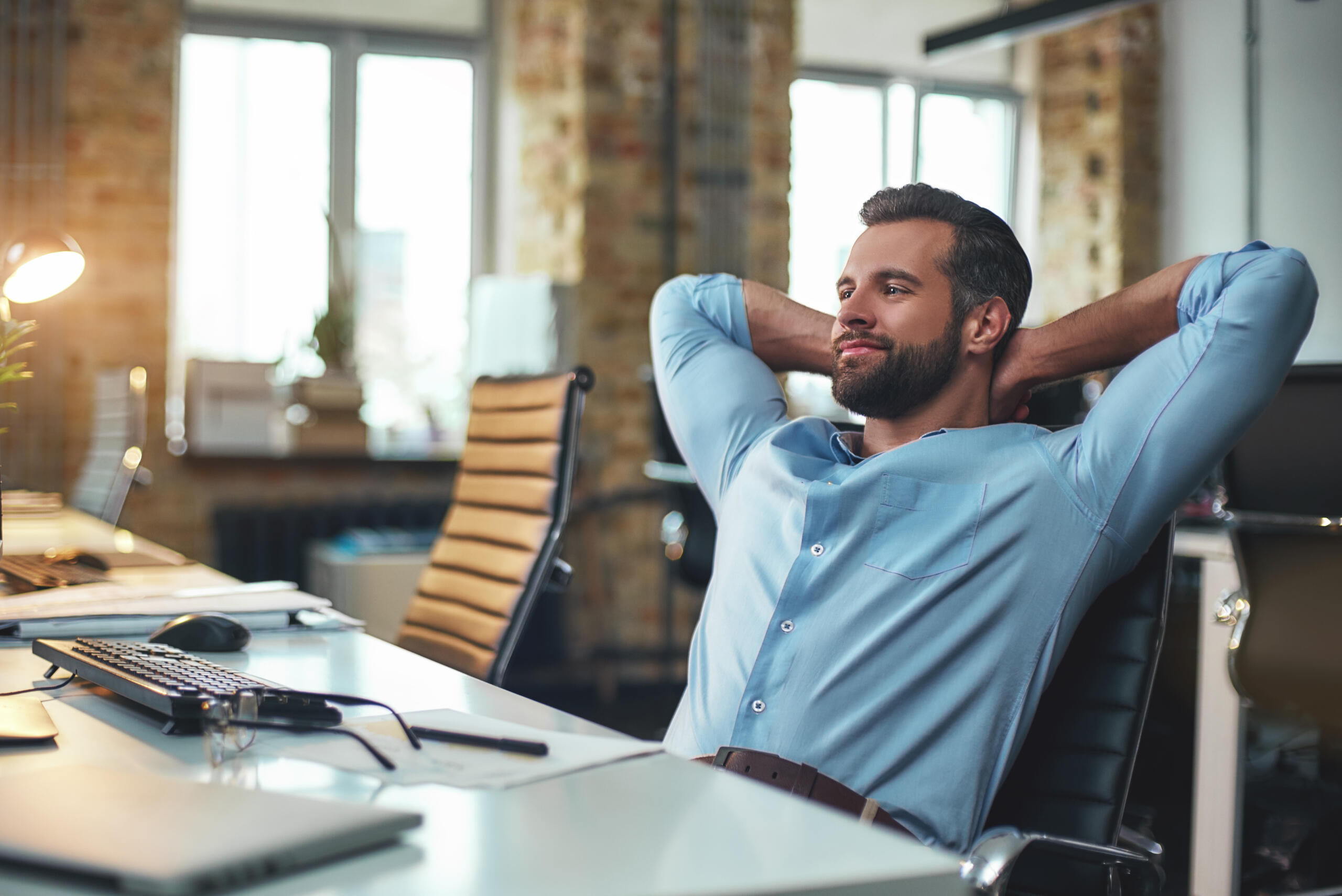 Small business exit strategy: business owner at desk with hands folded behind his head smiling