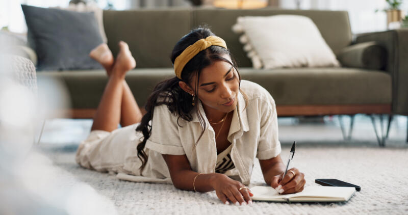 Small business productivity habits: woman lying on floor writing in notebook