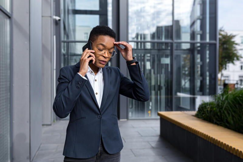 Has customer service gotten worse?: Person in suit looks frustrated while using the phone outside an office building