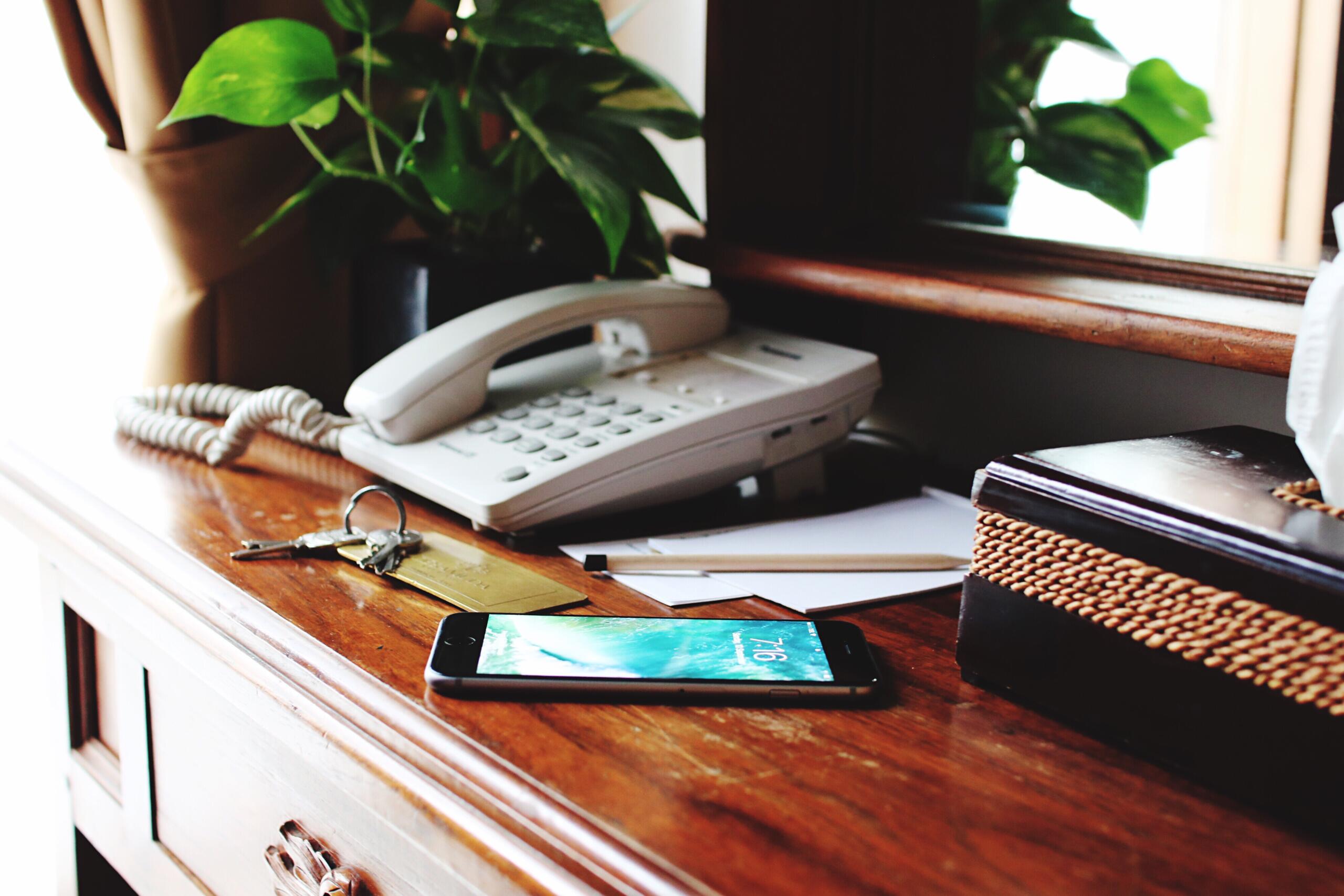 Why don't people answer the phone anymore: photo of cell phone with display lit up next to business phone on wooden surface